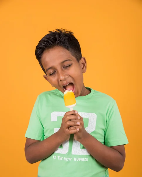 Kleine Indische jongen eten ijs lolly of ijs snoep, Indische jongen eten mango ijs, Aziatische jongen en oranje ijs snoep, geïsoleerd op gele achtergrond, 10 jaar jongen en ijs — Stockfoto
