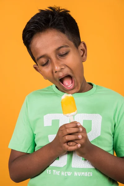 Kleine Indische jongen eten ijs lolly of ijs snoep, Indische jongen eten mango ijs, Aziatische jongen en oranje ijs snoep, geïsoleerd op gele achtergrond, 10 jaar jongen en ijs — Stockfoto