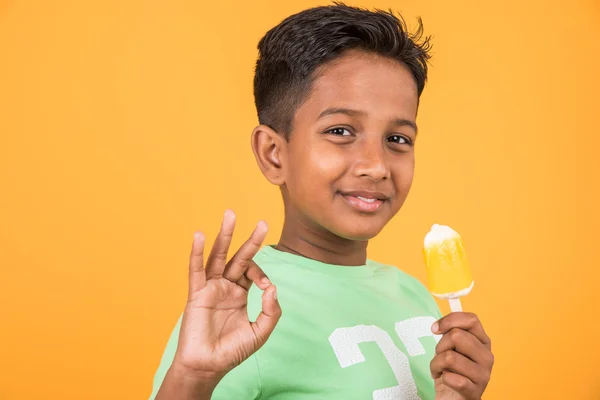 Kleiner indischer Junge isst Eislutscher oder Eisbonbons, indischer Junge isst Mango-Eis, asiatischer Junge und orangefarbene Eisbonbons, isoliert auf gelbem Hintergrund, 10-jähriger Junge und Eis — Stockfoto