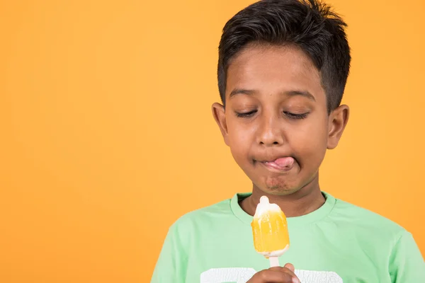 Kleine Indische jongen eten ijs lolly of ijs snoep, Indische jongen eten mango ijs, Aziatische jongen en oranje ijs snoep, geïsoleerd op gele achtergrond, 10 jaar jongen en ijs — Stockfoto