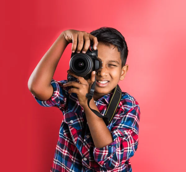 10 year old indian boy holding digital camera or DSLR camera, posing like a professional photographer, young photographer, kid photographer, child photographer, portrait, closeup, red background
