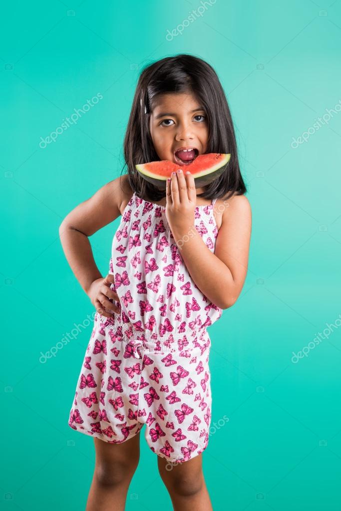 Indian child girl eating watermelon isolated on green background, asian  girl with a portion of the watermelon in her hands, small girl holding  watermelon, girl with black hair and watermelon, Stock Photo