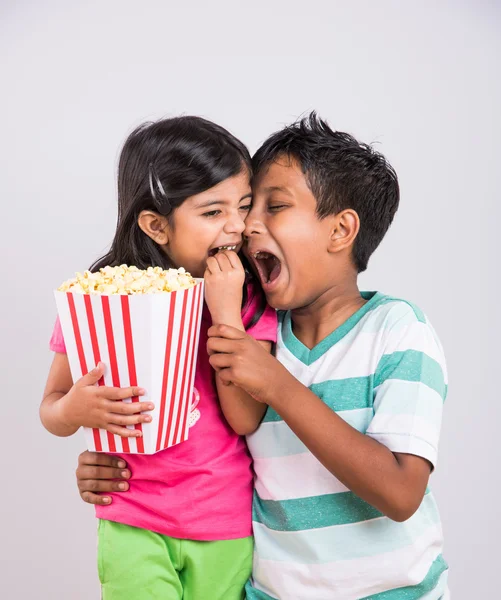 asian little boy and girl watching movie with pop corn, little indian girl sitting with brother watching movie eating popcorn, indian kids eating pop corn, kids watching movie with pop corn