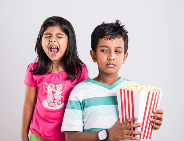 asian little boy and girl watching movie with pop corn, little indian girl sitting with brother watching movie eating popcorn, indian kids eating pop corn, kids watching movie with pop corn