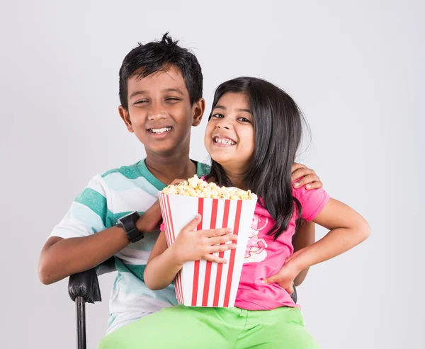 asian little boy and girl watching movie with pop corn, little indian girl sitting with brother watching movie eating popcorn, indian kids eating pop corn, kids watching movie with pop corn