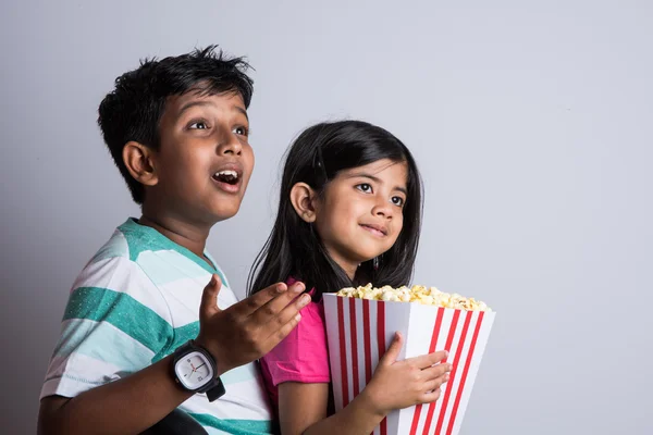 asian little boy and girl watching movie with pop corn, little indian girl sitting with brother watching movie eating popcorn, indian kids eating pop corn, kids watching movie with pop corn