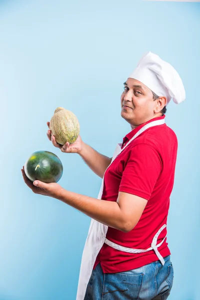 Guapo indio macho chef sosteniendo sandía y melón almizclero, asiático macho chef sosteniendo frutas, aislado sobre azul fondo — Foto de Stock