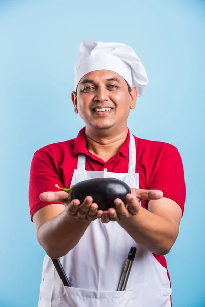 indian male chef holding fresh Cauliflower and spinach leaves, standing isolated over blue background, asian male chef holding fresh vegetables