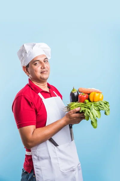Індійський чоловічий шеф-кухар тримає свіжі овочі в руці, азіатські чоловіки кухар кухар стояв з овочами, ізольовані на синьому фоні — стокове фото