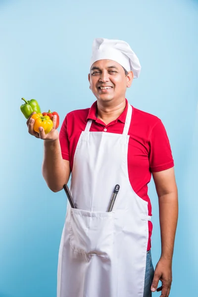 Indian Male chef showing capsicum , asian male cook chef and colorful capsicum, isolated over blue background — Stock Photo, Image