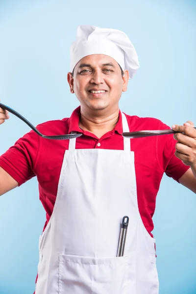 Молодий шеф-кухар тримає ложку скіммер і дерев'яну ложку ізольовано на синьому фоні — стокове фото