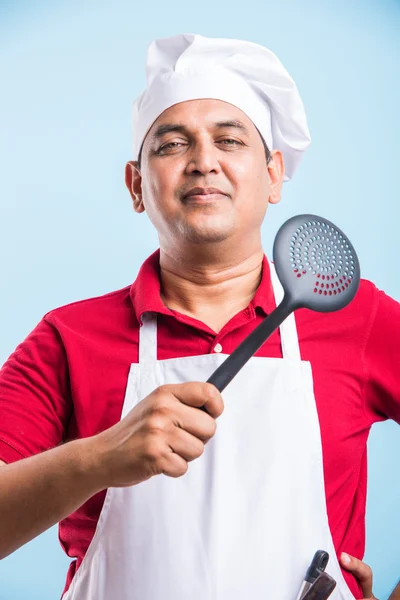 Молодой шеф-повар держит ложку обезжиренной и деревянную ложку изолированной на синем фоне — стоковое фото