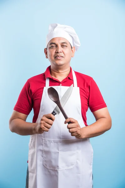 Багатозадачність є шеф-кухаря Гра. Крупним планом портрет красивий Індійська готувати проведення дерев'яні кулінарні ложкою і ополоник та ножем стоячи над синій фону з копію простору, азіатські чоловічого шеф-кухаря — стокове фото