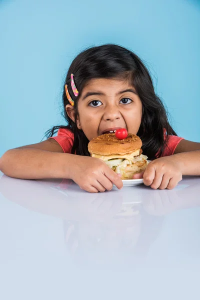 cute indian girl eating burger, small asian girl and burger, isolated over yellow background