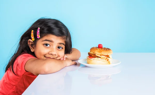 Söt indisk flicka som äter hamburgare, liten asiatisk tjej och hamburgare, isolerad över gul bakgrund — Stockfoto