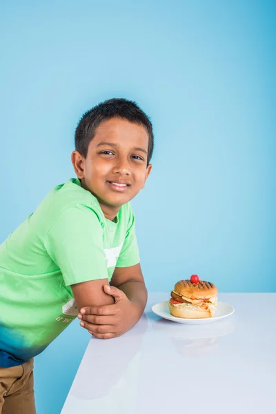 Schattige Indiase jongen en Hamburger in kleine witte plaat, kleine Aziatische jongen en Hamburger, over kleurrijke achtergrond — Stockfoto
