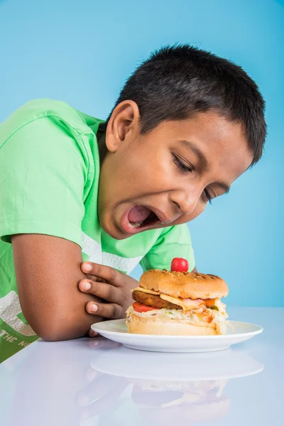 Schattige Indiase jongen en Hamburger in kleine witte plaat, kleine Aziatische jongen en Hamburger, over kleurrijke achtergrond — Stockfoto