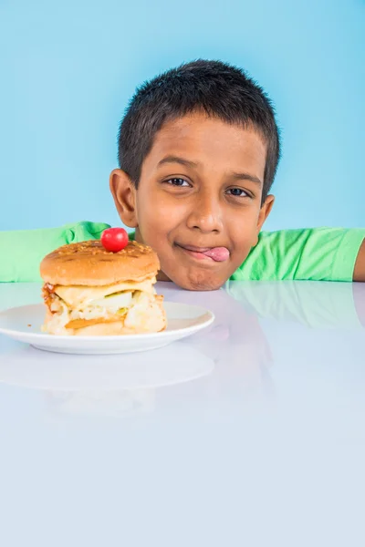 Schattige Indiase jongen en Hamburger in kleine witte plaat, kleine Aziatische jongen en Hamburger, over kleurrijke achtergrond — Stockfoto