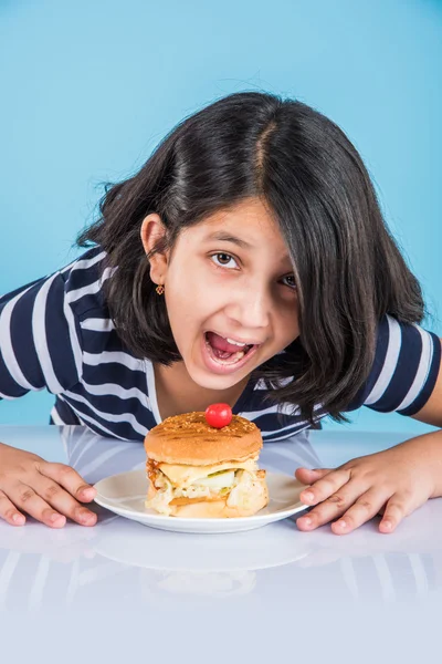 cute indian girl eating burger, small asian girl and burger, isolated over colourful background