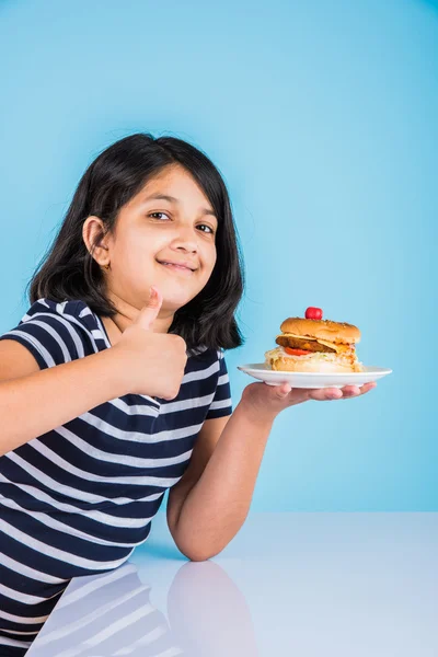 Schattig Indiase meisje eten hamburger, klein Aziatisch meisje en Hamburger, geïsoleerd op kleurrijke achtergrond — Stockfoto