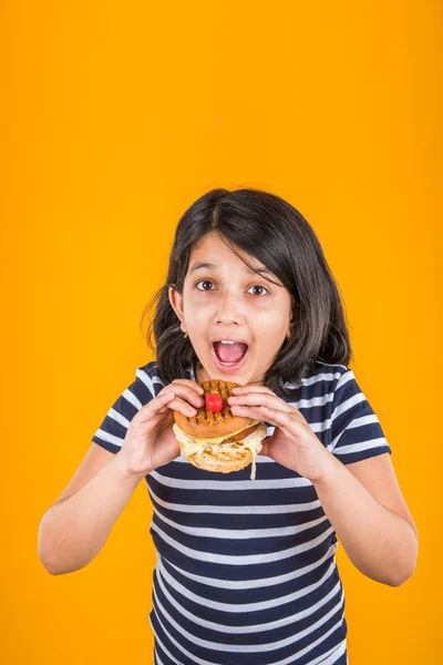Schattig Indiase meisje eten hamburger, klein Aziatisch meisje en Hamburger, geïsoleerd op kleurrijke achtergrond — Stockfoto