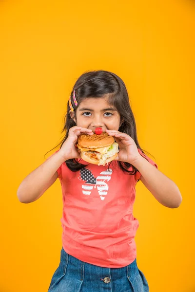 Schattig Indisch meisje eten hamburger, kleine Aziatische meisje en Hamburger, geïsoleerd over gele achtergrond — Stockfoto