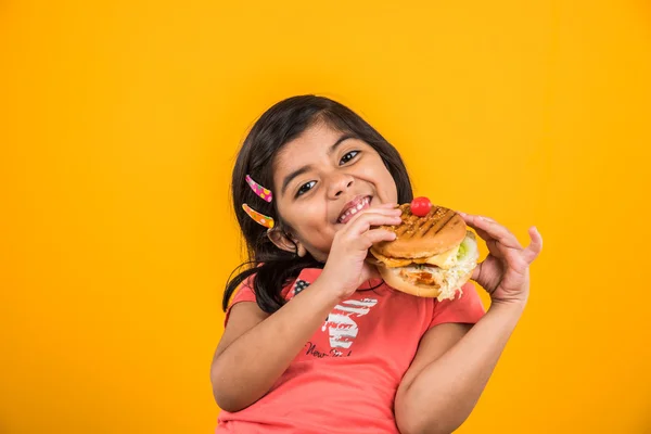 cute indian girl eating burger, small asian girl and burger, isolated over yellow background