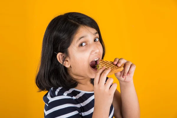 indian girl eating sandwich, asian girl and sandwich, cute indian girl posing with sandwich on yellow background