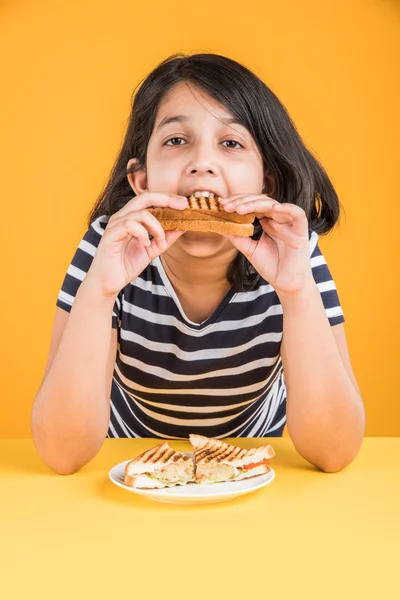 indian girl eating sandwich, asian girl and sandwich, cute indian girl posing with sandwich on yellow background