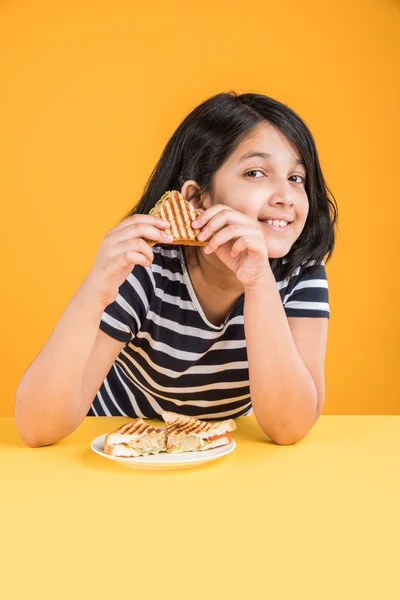 indian girl eating sandwich, asian girl and sandwich, cute indian girl posing with sandwich on yellow background