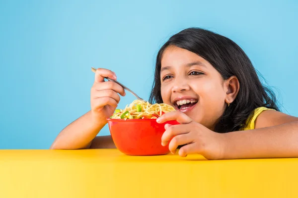 Gelukkig Aziatisch kind eten heerlijke noodle, kleine Indiase meisje eten noedels in rode kom, over blauwe achtergrond — Stockfoto