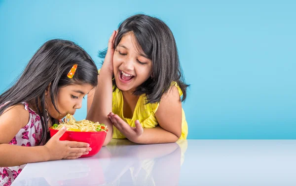 Crianças asiáticas felizes comendo delicioso macarrão, duas meninas indianas alegres comendo macarrão em tigela vermelha sobre fundo azul, duas irmãzinhas indianas ou amigos com macarrão — Fotografia de Stock