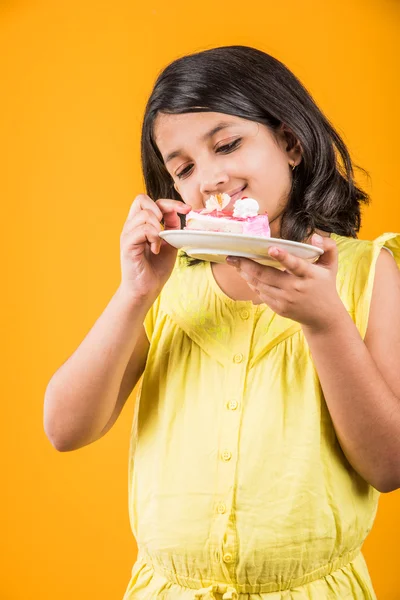Портрет индийского ребенка, поедающего торт или выпечку, милая маленькая девочка, поедающая торт, девушка, поедающая клубничный торт на желтом фоне — стоковое фото