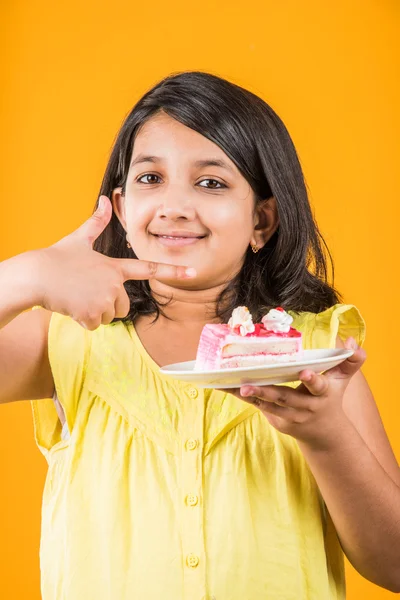 Retrato de criança indiana comendo bolo ou pastelaria, linda menina comendo bolo, menina comendo bolo de morango sobre fundo amarelo — Fotografia de Stock