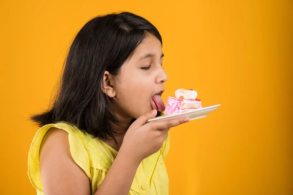 portrait of Indian kid eating cake or pastry, cute little girl eating cake, girl eating strawberry cake over yellow background
