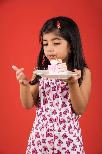 portrait of Indian kid eating cake or pastry, cute little girl eating cake, girl eating strawberry cake over red background