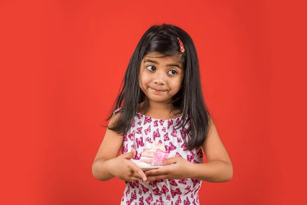Retrato de niño indio comiendo pastel o pastelería, linda niña comiendo pastel, niña comiendo pastel de fresa sobre fondo rojo —  Fotos de Stock