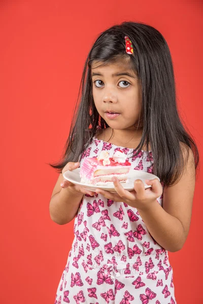 portrait of Indian kid eating cake or pastry, cute little girl eating cake, girl eating strawberry cake over red background