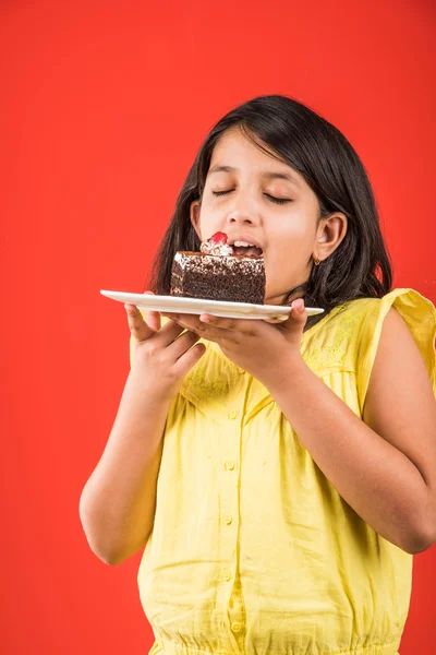 Portret van Indiase Kid eten cake of gebak, schattige kleine meisje eten cake, meisje eten chocolade taart of gebak over kleurrijke achtergrond — Stockfoto