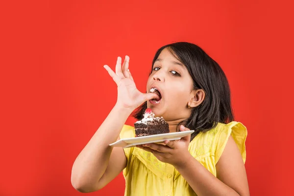 Portret van Indiase Kid eten cake of gebak, schattige kleine meisje eten cake, meisje eten chocolade taart of gebak over kleurrijke achtergrond — Stockfoto