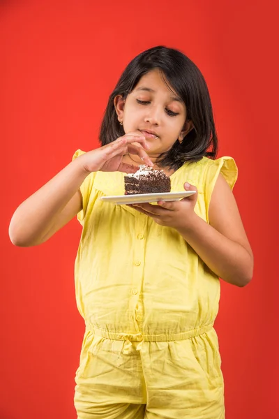 Portret van Indiase Kid eten cake of gebak, schattige kleine meisje eten cake, meisje eten chocolade taart of gebak over kleurrijke achtergrond — Stockfoto