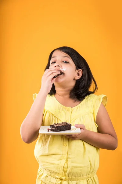 Retrato de criança indiana comendo bolo ou pastelaria, linda menina comendo bolo, menina comendo bolo de chocolate ou pastelaria sobre fundo colorido — Fotografia de Stock