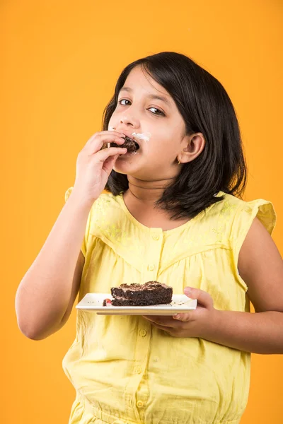 Portret van Indiase Kid eten cake of gebak, schattige kleine meisje eten cake, meisje eten chocolade taart of gebak over kleurrijke achtergrond — Stockfoto