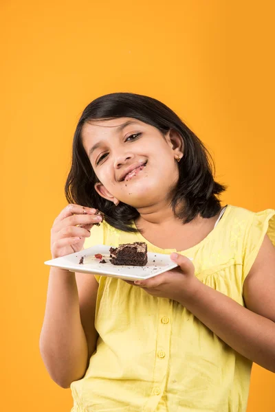 Portret van Indiase Kid eten cake of gebak, schattige kleine meisje eten cake, meisje eten chocolade taart of gebak over kleurrijke achtergrond — Stockfoto