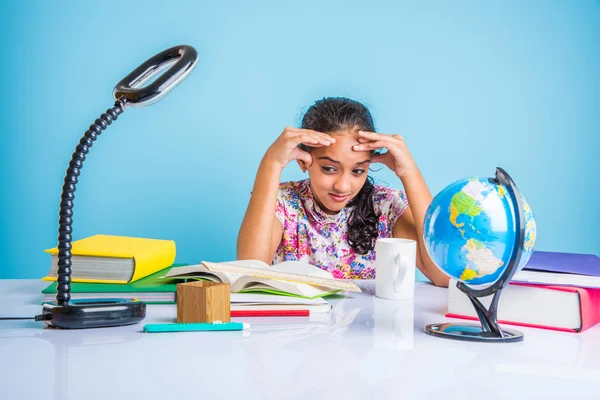 education and home concept - stressed student girl with books, indian girl child tired of studying or doing homework, asian girl studying and stressed, with globe toy and coffee mug