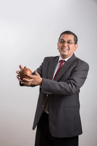 happy indian businessman man holding piggy bank or money box made up of clay, clay money box & asian business man, isolated over white background, indian man with piggy bank, money box