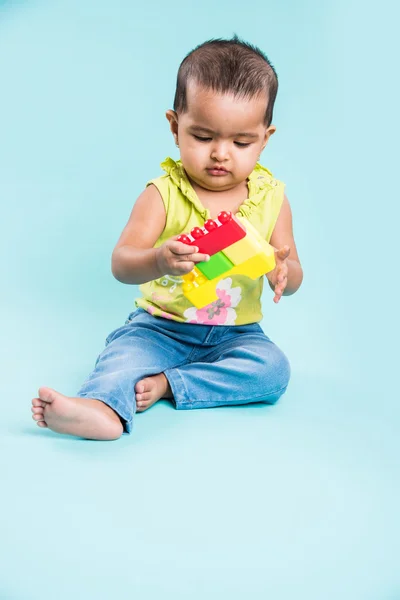 indian baby girl playing with toys or blocks or soft toys over blue background, asian infant playing with toys, indian toddler playing indoor