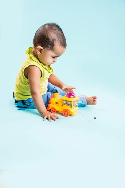 indian child playing with colourful toy. Isolated on blue background, indian girl playing with engine toy, asian girl playing with colourful toy engine