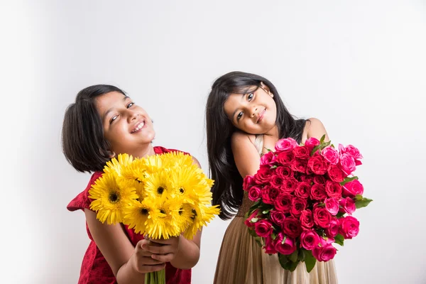 two cute indian little girls holding flower bouquet, two small girls with gerbera and rose bouquet, isolated on white