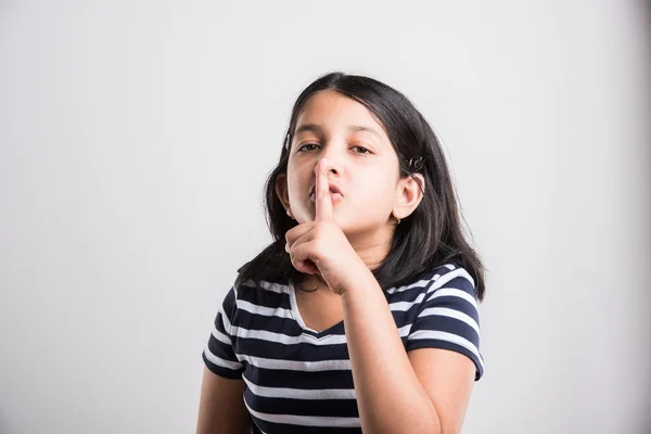 Beautiful indian little girl putting finger up to lips & ask silence onwhite background. asian girl child doing a Please Keep Quiet gesture towards the camera, indian small girl & silence please sign